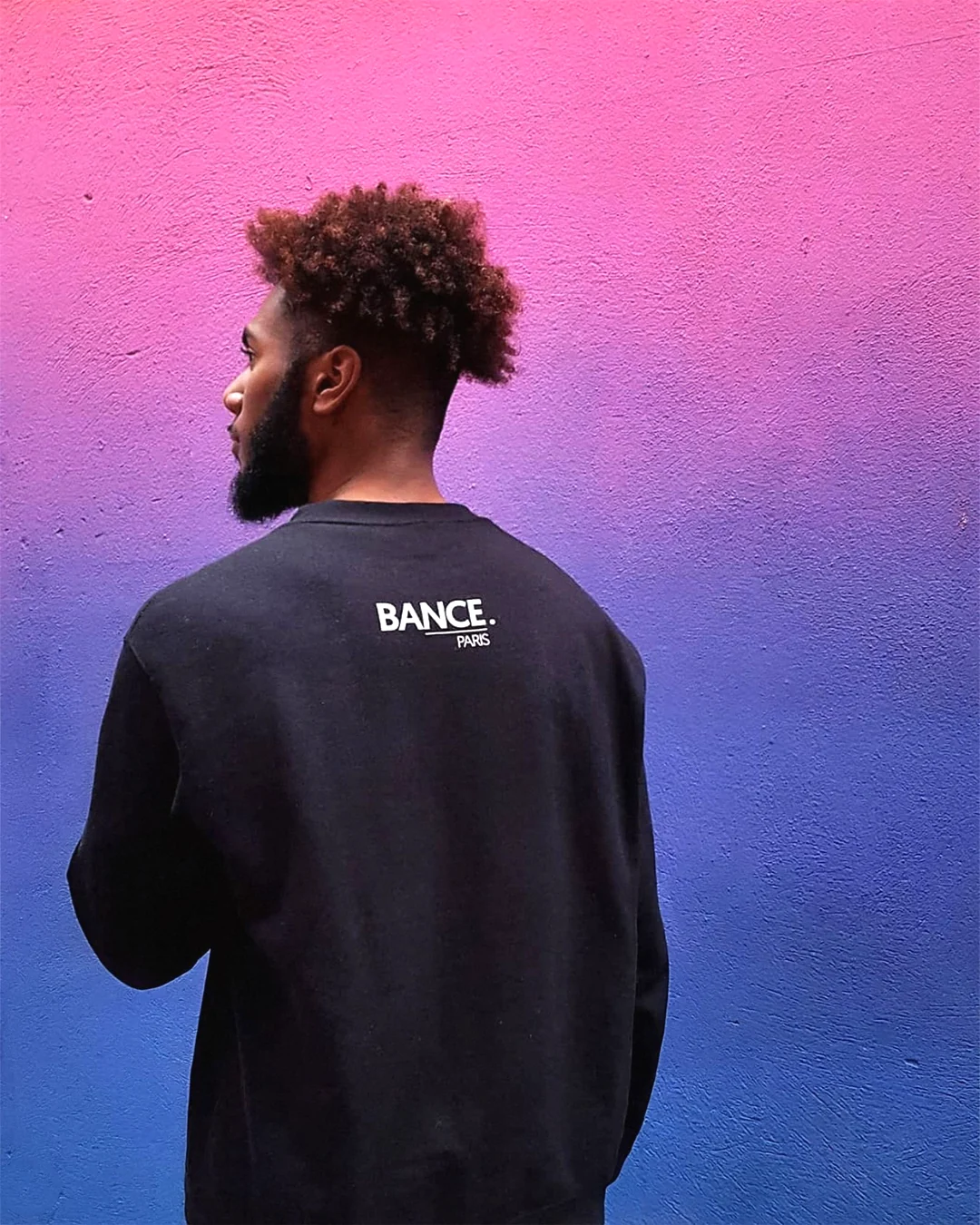 Dany de dos, en sweat noir Bance Paris, au terrain de basket de Pigalle